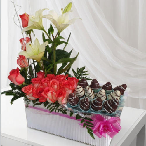 Arreglo floral en caja rectangular con rosas rojas, lirios blancos, follaje verde y fresas cubiertas de chocolate en Quito.