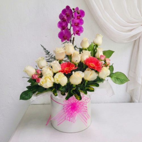 Arreglo floral en base elegante con una plantas de orquídeas, rosas, gerberas y follaje verde primaveral en Quito.